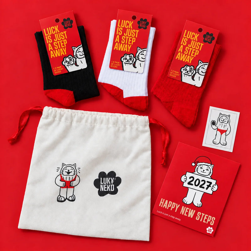 Lucky Bag 2027 by LukyNeko: three pairs of lucky socks, the Happy New Steps card and the cotton bag, flat lay on red